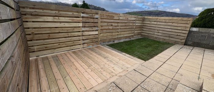 Horizontal hit and miss fencing with a matching gate around a wooden decking that is flush with grass and a patio