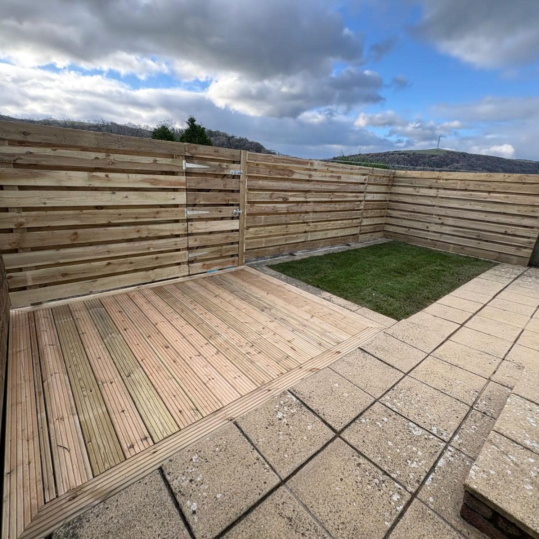 Horizontal hit and miss fencing with a matching gate around a wooden decking that is flush with grass and a patio